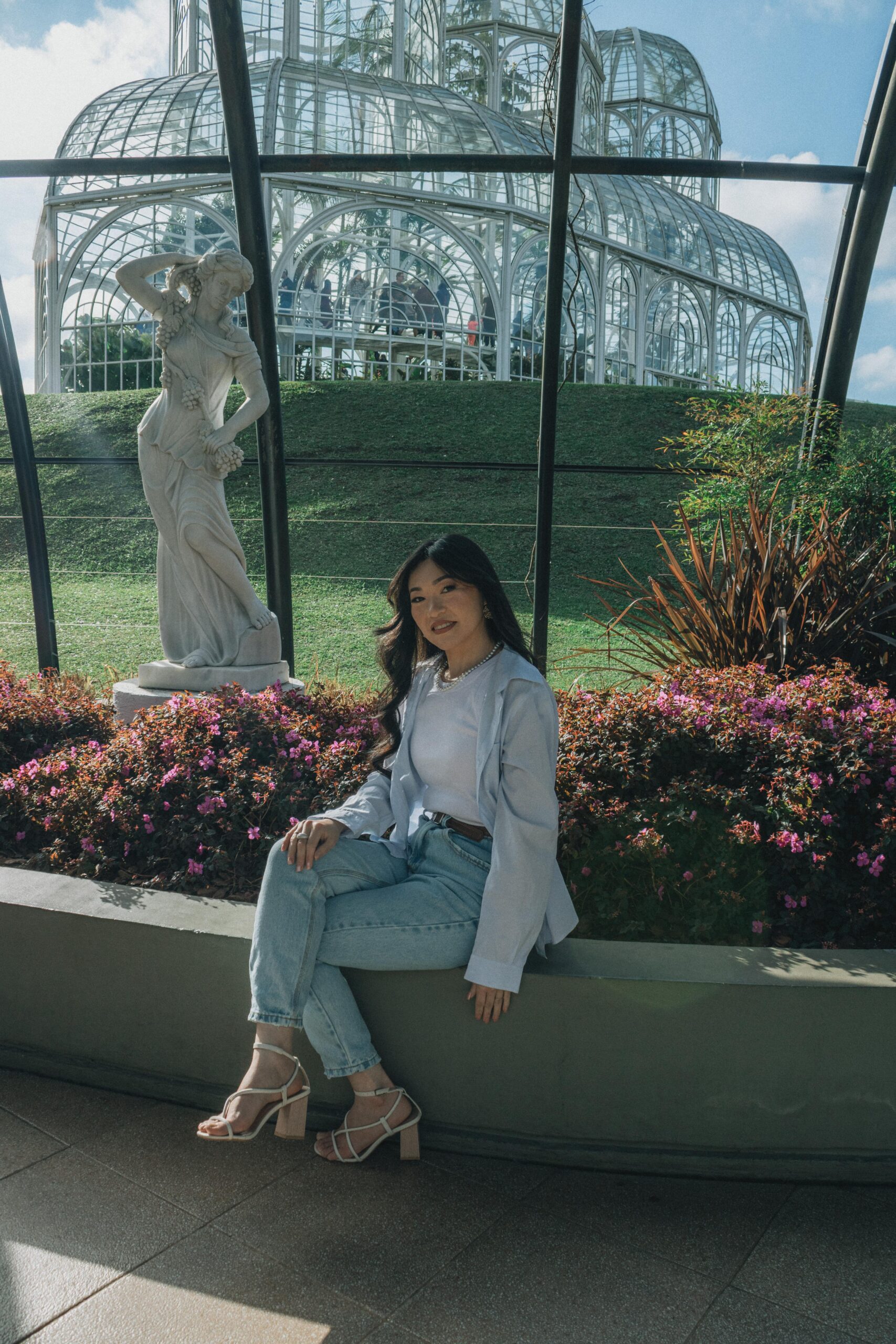 Young woman sitting by flowers in a glasshouse. Sunny day, natural beauty captured in a botanical setting.