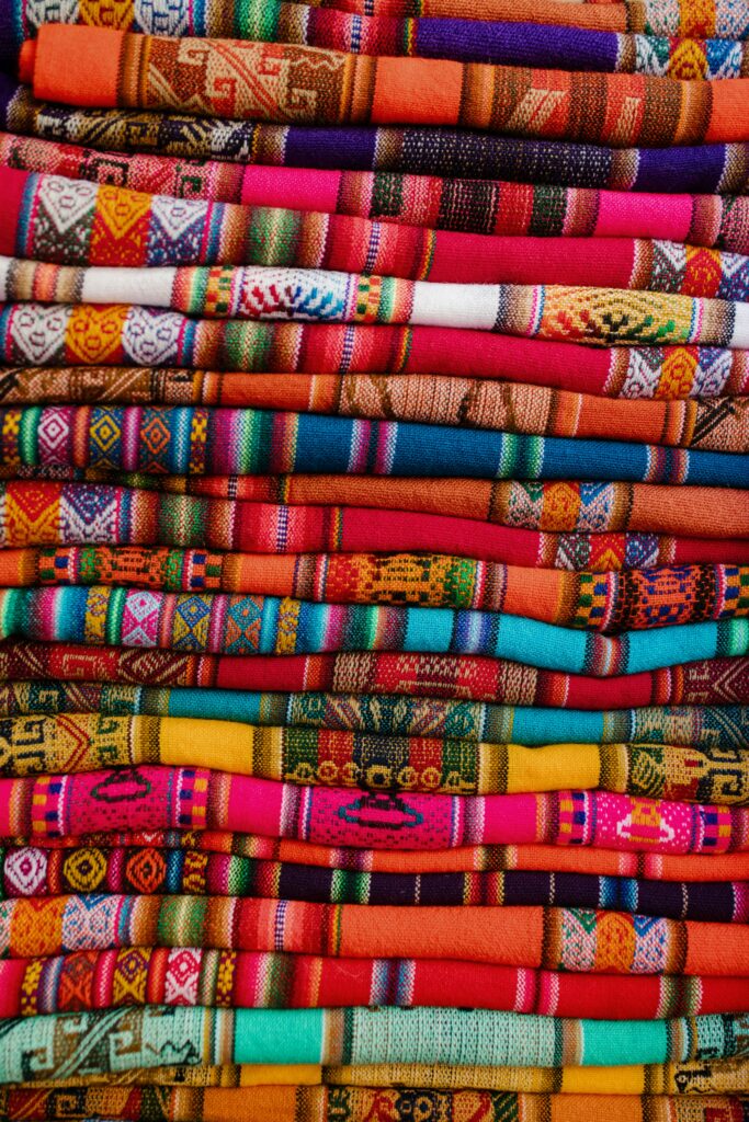 pexels photo 5656671 5656671 Vibrant, handwoven Peruvian fabrics intricately folded in a vertical arrangement showcasing cultural motifs.
